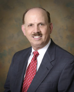 Attorney and Author headshot sitting in dark suit against a tan background