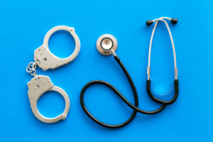 Medical lawsuit. Arrest for medical crime concept. Handcuff near stethoscope on blue background top view.